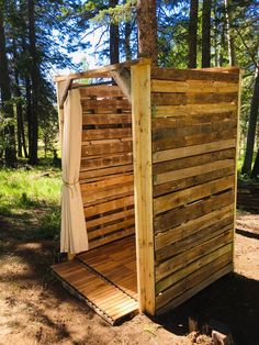 a small wooden structure in the woods with curtains on it's sides and an open door