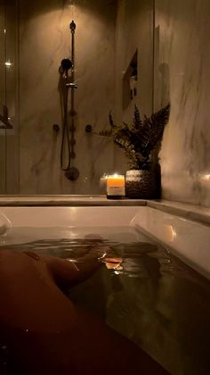 a person in a bathtub with candles on the side and a plant next to it