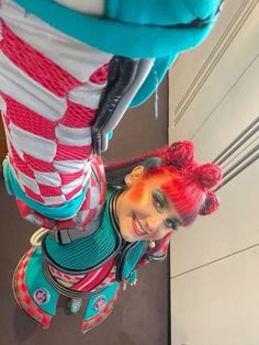 a woman with red hair and makeup is standing in front of a mirror wearing colorful clothing