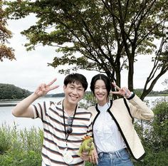 two people standing next to each other in front of a tree with their hands up