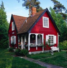 a red house with white trim and windows on the front porch is surrounded by greenery