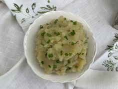 a white bowl filled with mashed potatoes and green onions