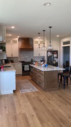 an open kitchen and dining room area with hardwood flooring, white cabinets, stainless steel appliances and pendant lights