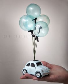 a small toy car with balloons attached to it's head is held by a hand