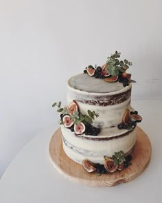 a three tiered cake with figs and flowers on the top is sitting on a wooden platter