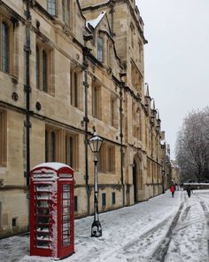 a red phone booth sitting on the side of a snow covered street next to tall buildings