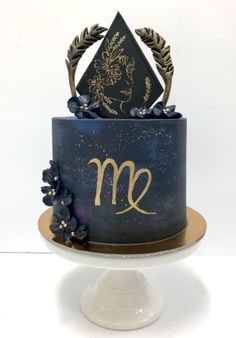 a blue and gold cake with the letter m on it's side, decorated with flowers