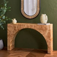 a table with a mirror and vases on it in front of a green wall