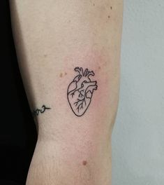 a small heart tattoo on the left side of the arm is shown in black ink