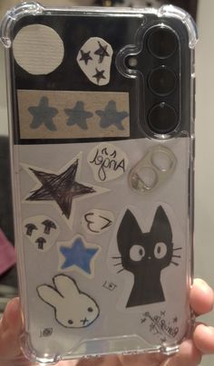 someone is holding up their phone case with stickers on it, and there are other things in the back