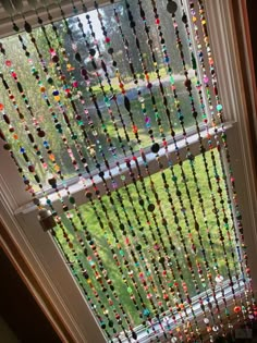 a window with beads hanging from it's side and a green yard in the background