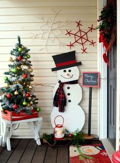 a snowman with a hat and scarf next to a christmas tree on the porch