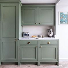 a kitchen with green cupboards and white counter tops, along with a coffee maker