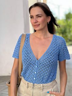 a woman in blue shirt and tan pants holding a brown handbag while standing next to a building