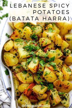 a white plate topped with potatoes and parsley next to a fork on a table