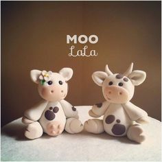 two ceramic cows sitting next to each other on top of a white tablecloth with the words moo tat written above them