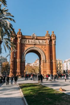 the arch of triumph in barcelona, spain with people walking and sitting on the grass