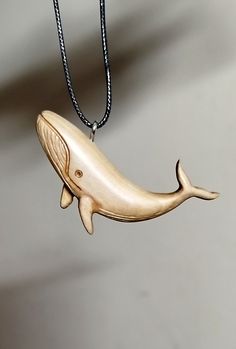 a wooden whale necklace hanging from a black cord on a gray surface with a white wall in the background