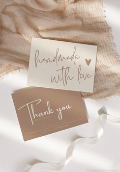 two thank cards sitting next to each other on top of a white cloth covered blanket