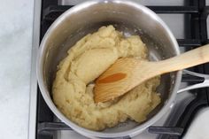 a wooden spoon stirring mashed potatoes in a saucepan on the stove with a white counter top