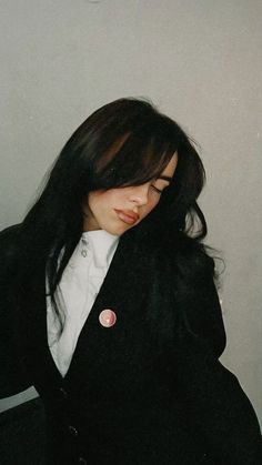 a woman with long black hair wearing a jacket and white shirt is leaning against a wall