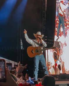 a man with a cowboy hat and guitar on stage in front of a large crowd