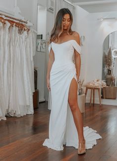 a woman in a white dress standing on a wooden floor next to a rack of wedding dresses