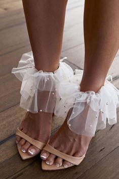 a close up of a person's legs wearing high heeled sandals with ruffles and pearls