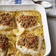 four fish fillets in a white casserole dish with lemon slices and spices