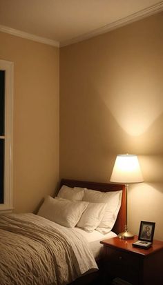 a bed sitting under a window next to a night stand with a lamp on it