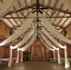 the inside of a barn decorated with white draping and fairy lights on the ceiling