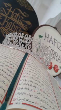 an open book with arabic writing and a tiara on top of it, surrounded by other books