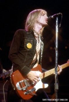 a man with long hair playing an electric guitar in front of a microphone on stage