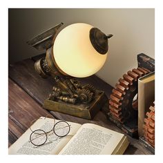 an open book sitting on top of a wooden table next to a lamp and eye glasses