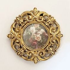 an ornate gold frame with flowers in it on a white wall behind a small mirror