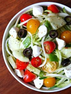 a white bowl filled with cucumber, tomatoes, olives and other veggies