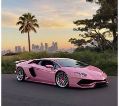 a pink sports car parked in front of a palm tree with the city skyline behind it