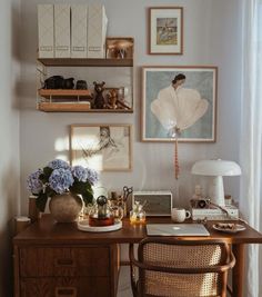 a wooden desk topped with a laptop computer next to a lamp and pictures on the wall