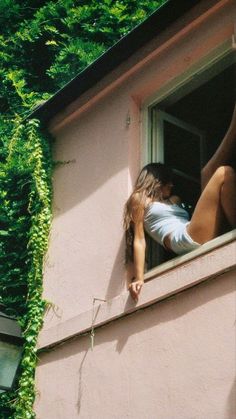 a woman leaning out the window of a pink building with ivy growing on it's side