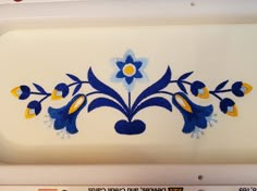 a white tray with blue and yellow designs on the side, sitting on top of a shelf