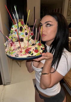 a woman holding a cake with candles on it in front of her face and looking at the camera