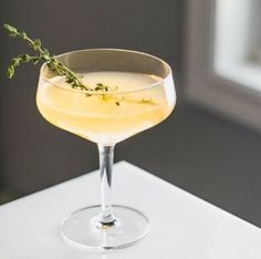 a drink in a wine glass with a sprig of thyle on the rim