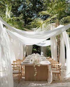 an outdoor dining area with white draping and wooden tables