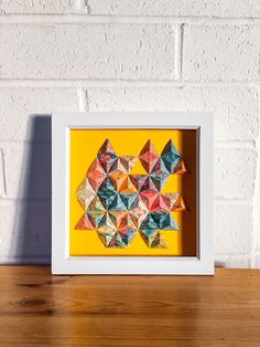 an origami art piece in a white frame on a wooden table