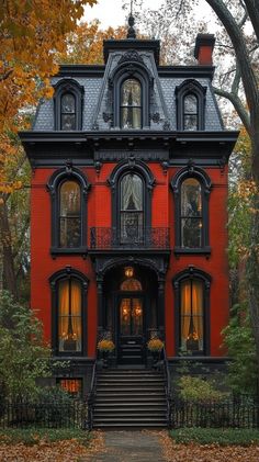 a red house with black trim and windows on the front porch is surrounded by trees