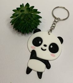 a panda bear keychain sitting next to a green plant on a white surface