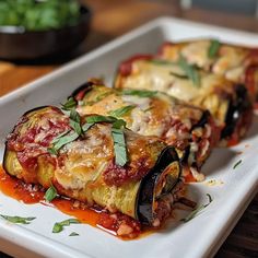 three stuffed eggplant rolls on a plate covered in sauce and garnished with fresh herbs