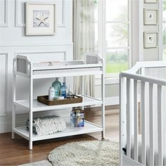 a baby crib in a white nursery with lots of items on the shelves and floor