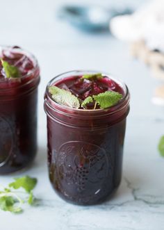 two jars filled with liquid sitting on top of a white table next to green leaves