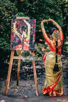 a woman is standing in front of an easel and holding her hands up to the painting